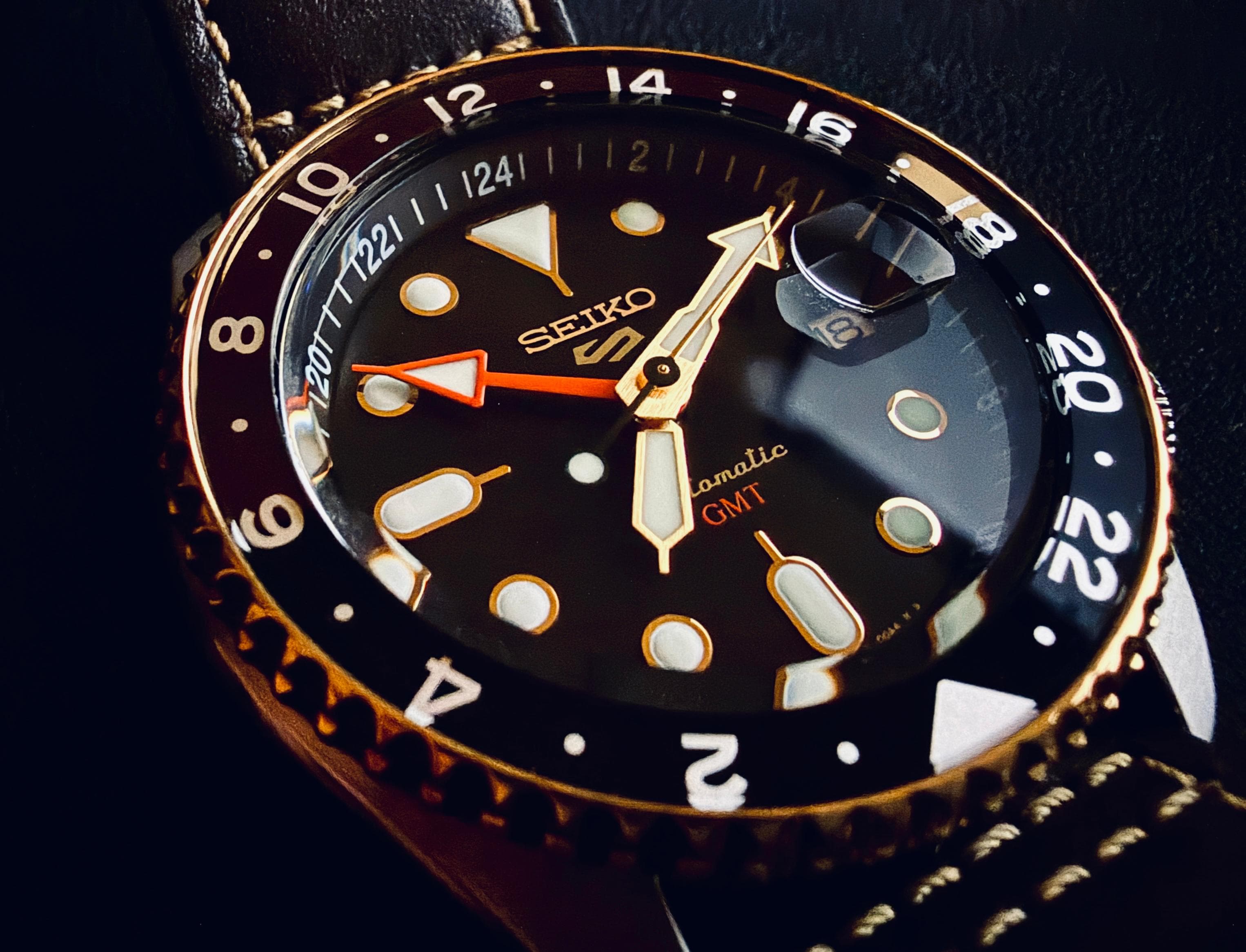 Macro shot of a Seiko 5 Sports GMT watch, orange hand crossing a dark dial on a leather strap